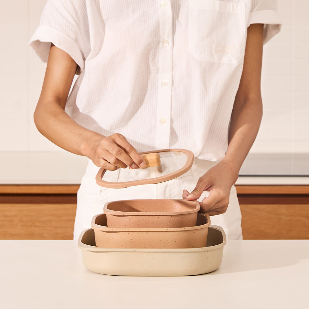 Person placing a glass lid with a wooden handle onto a set of terracotta and beige containers.