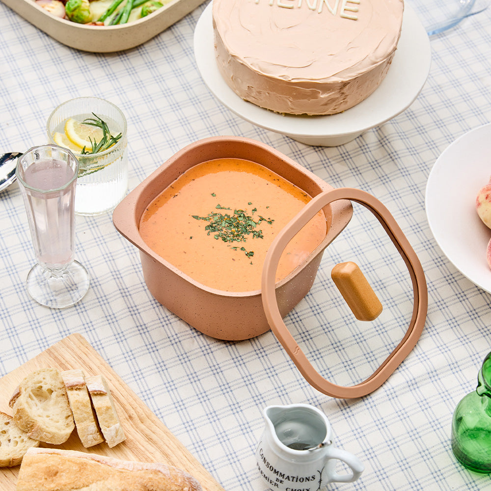 Terracotta container filled with soup, displayed with bread and drinks on a dining table.