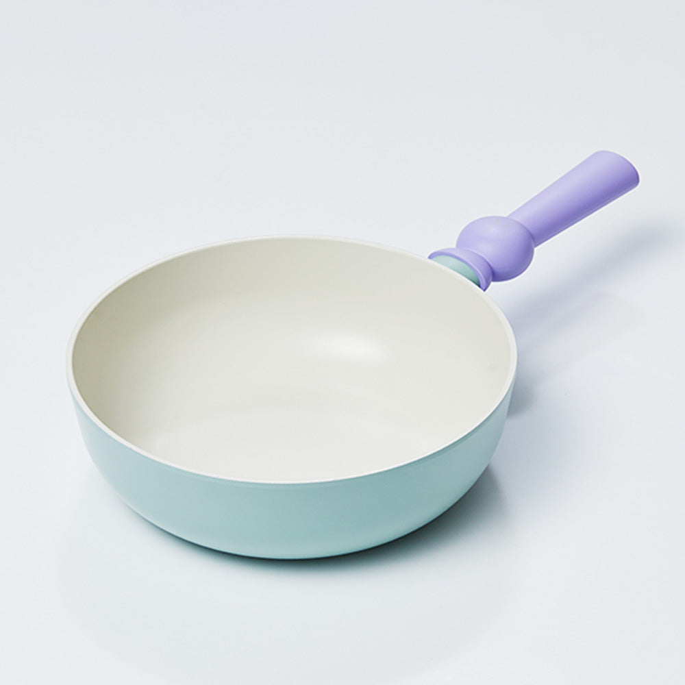 A pastel-colored wok with a light green body and a purple handle, displayed on a white background