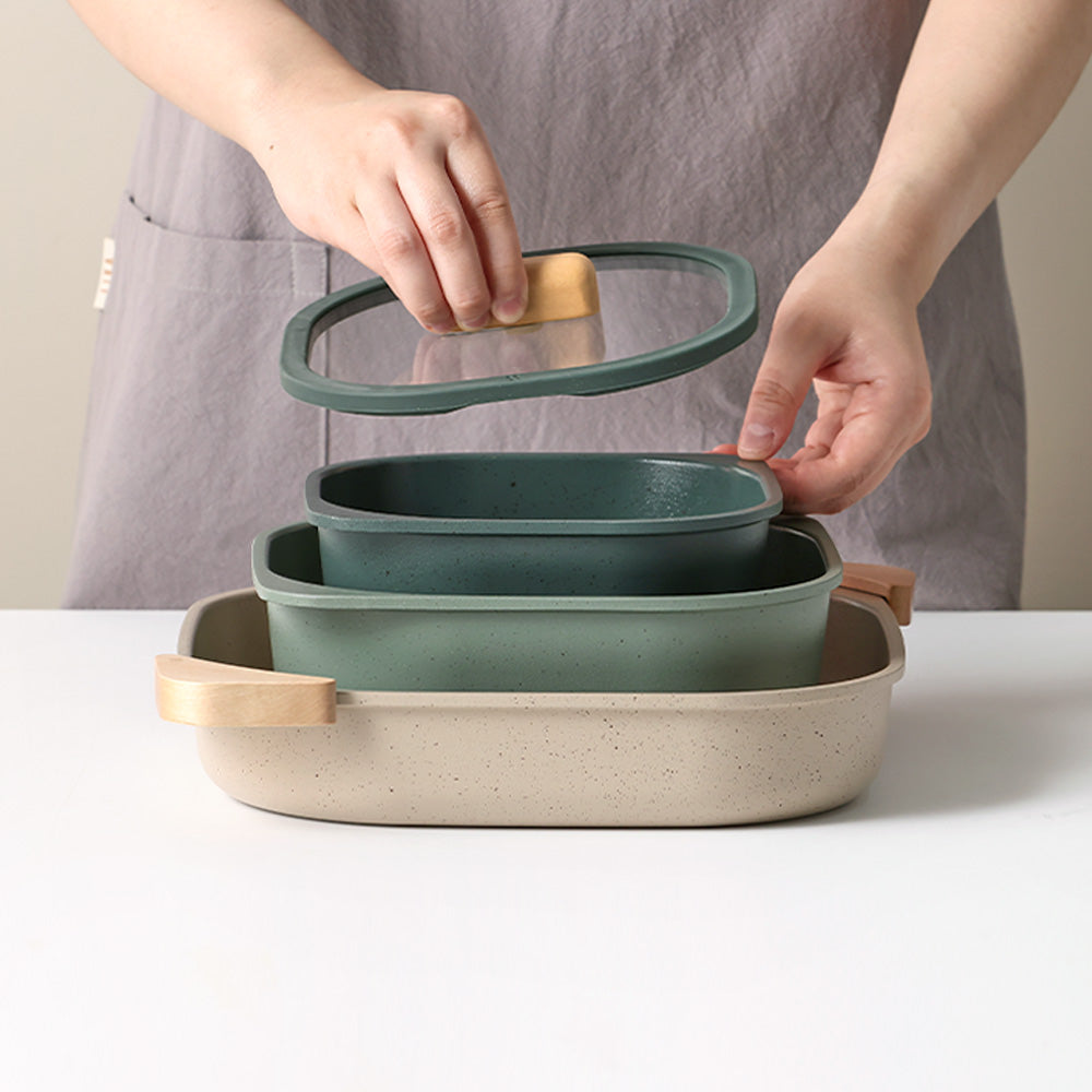 Person placing a glass lid with a wooden handle onto a stacked set of green and beige containers.